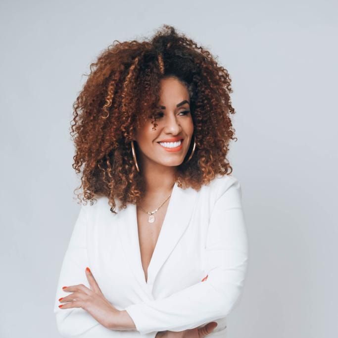 Cassia Aschidamini, diretora da ASKID, sorrindo, de blazer branco e braços cruzados.